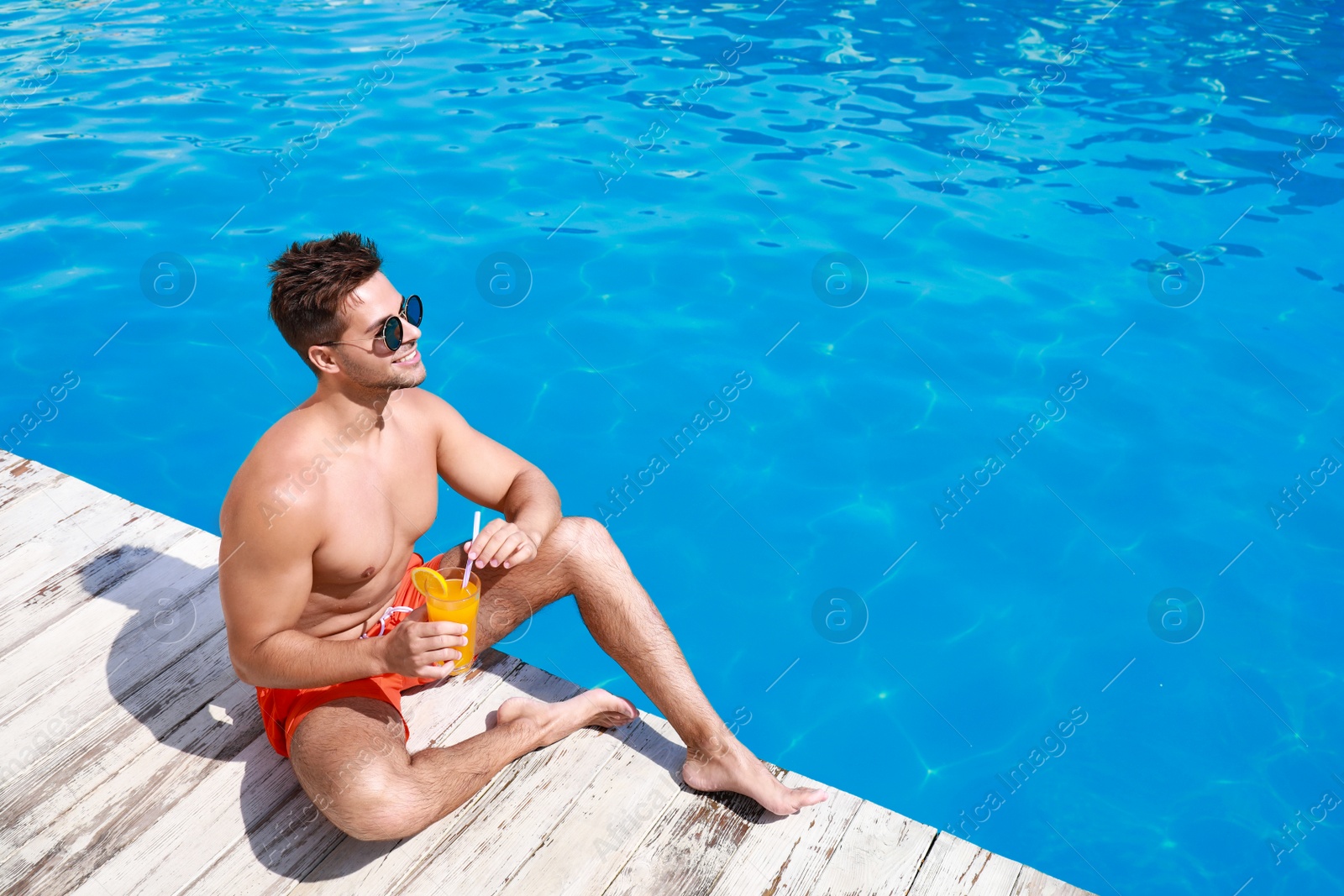 Photo of Handsome young man with refreshing cocktail near swimming pool on sunny day. Space for text