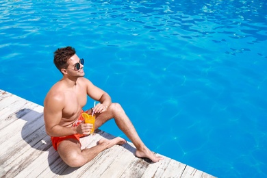 Handsome young man with refreshing cocktail near swimming pool on sunny day. Space for text