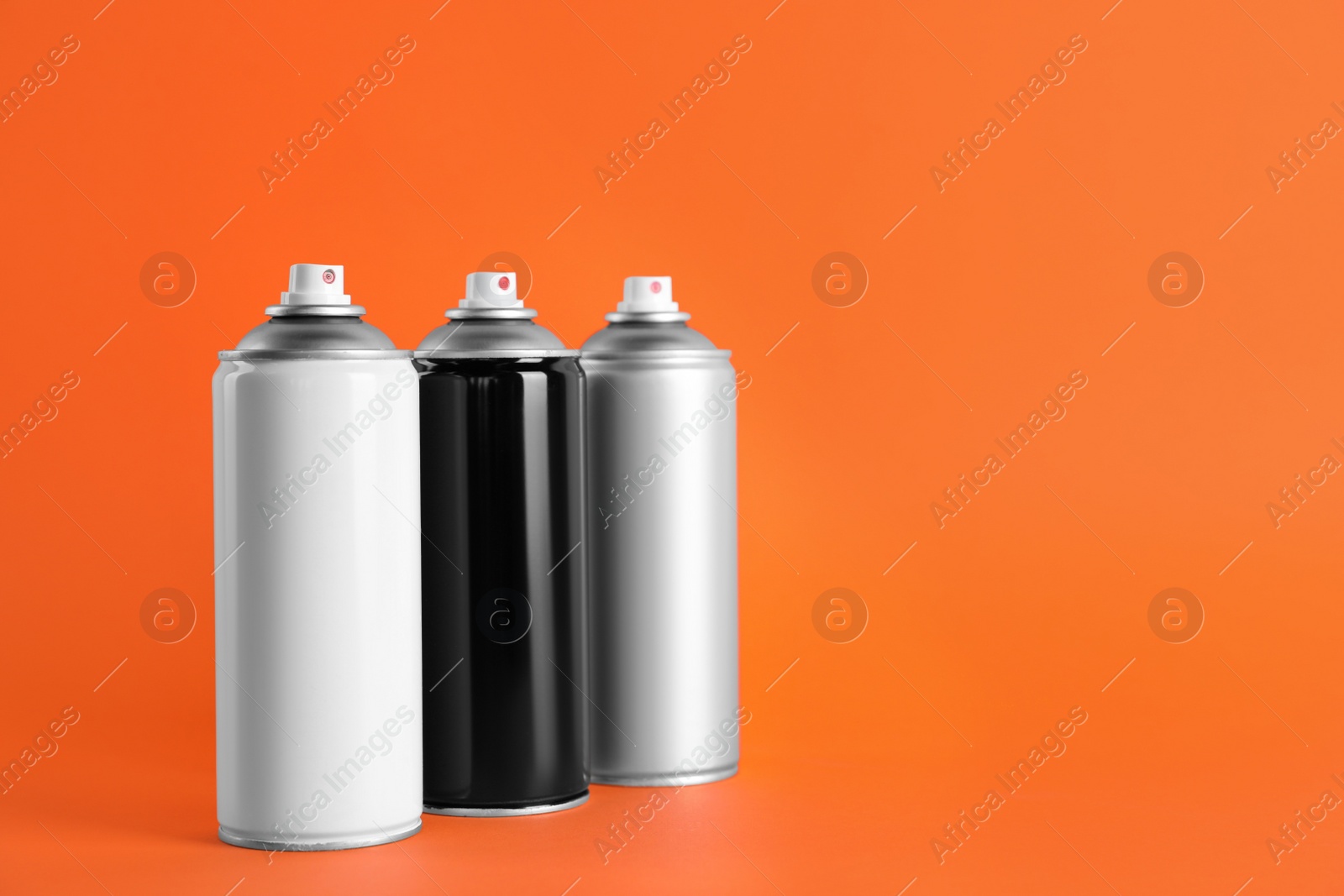 Photo of Cans of spray paints on orange background. Space for text