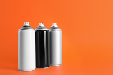 Photo of Cans of spray paints on orange background. Space for text
