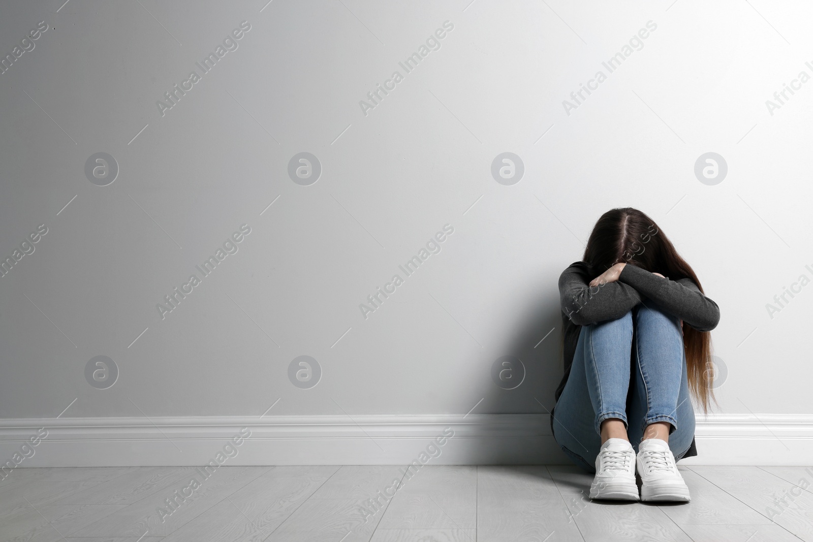 Photo of Upset teenage girl sitting on floor near wall. Space for text