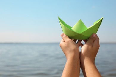 Photo of Child holding green paper boat near river, closeup. Space for text