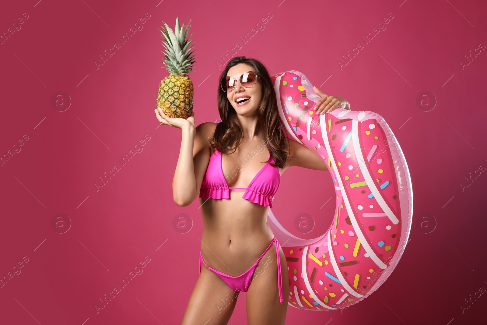 Photo of Beautiful woman in stylish bikini with inflatable ring and pineapple on crimson background