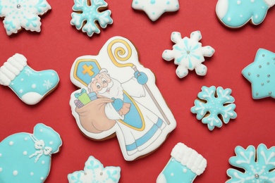 Photo of Tasty gingerbread cookies on red background, flat lay. St. Nicholas Day celebration