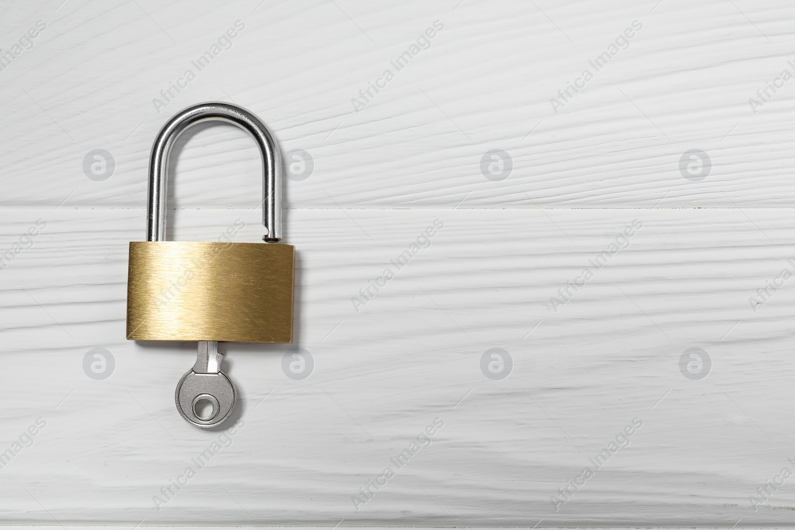 Photo of Steel padlock with key on white wooden table, top view. Space for text