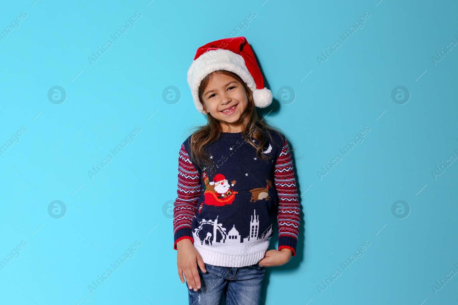 Photo of Cute little girl in Christmas sweater and hat on color background