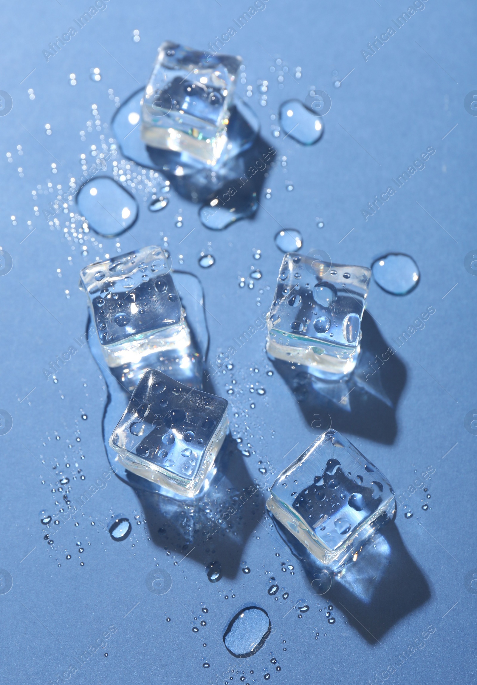 Photo of Melting ice cubes and water drops on blue background, flat lay