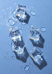 Melting ice cubes and water drops on blue background, flat lay