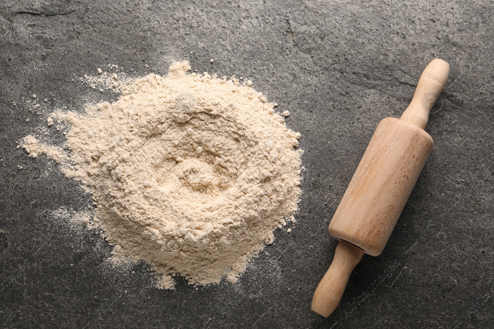 Photo of Pile of flour and rolling pin on grey textured table, top view