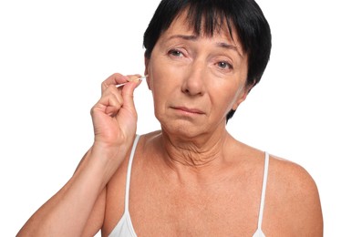 Senior woman cleaning ear with cotton swab on white background