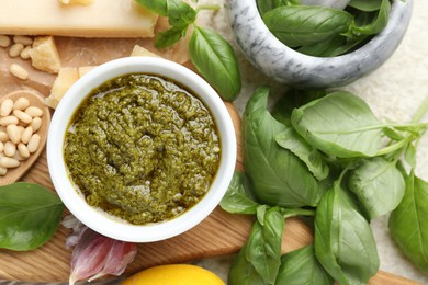 Photo of Tasty pesto sauce in bowl, basil, pine nuts, garlic and cheese on table, top view