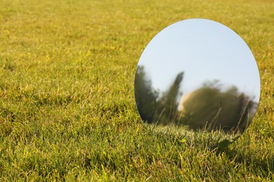 Photo of Round mirror on grass reflecting trees and sky. Space for text