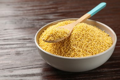 Photo of Millet groats in bowl and spoon on wooden table, closeup. Space for text