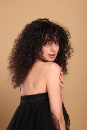 Beautiful young woman with long curly hair on beige background