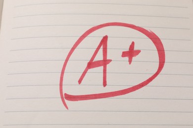 School grade. Red letter A with plus symbol on notebook paper, top view