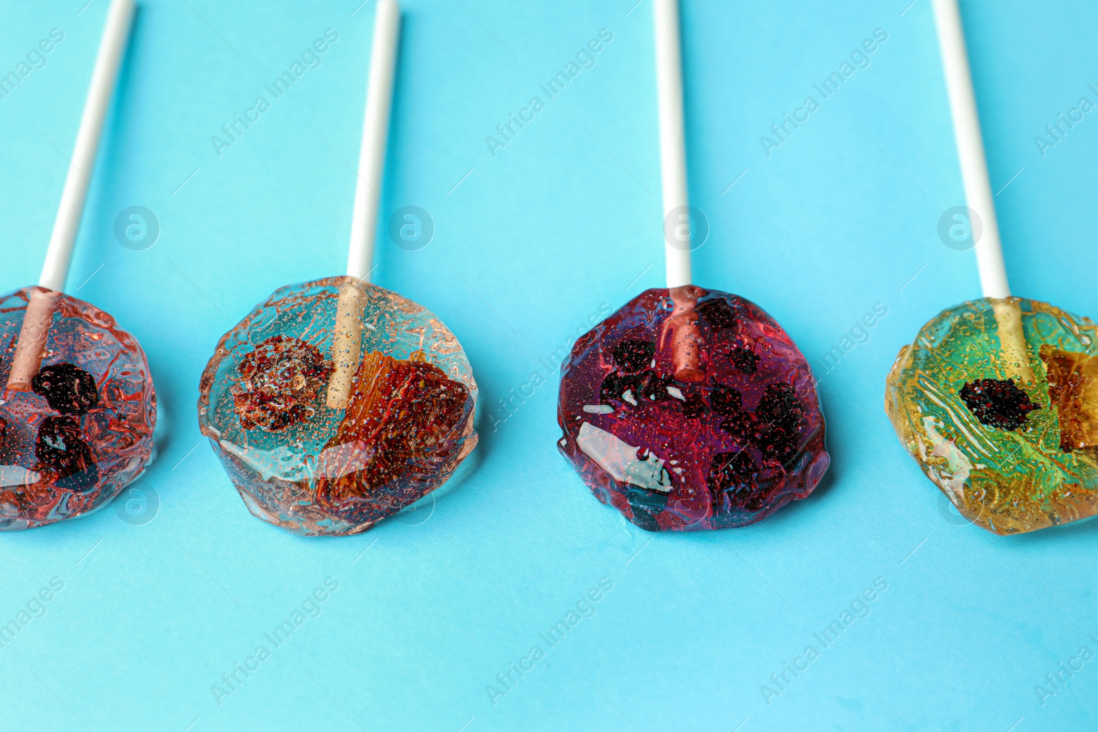 Photo of Sweet colorful lollipops with berries on light blue background, closeup. Space for text