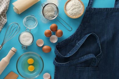 Photo of Denim apron, different ingredients and kitchen tools on light blue background, flat lay