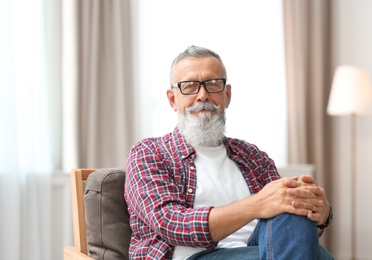 Photo of Portrait of handsome mature man with glasses sitting on chair in room