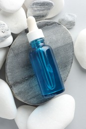 Bottle of face serum and stones on light grey background, top view