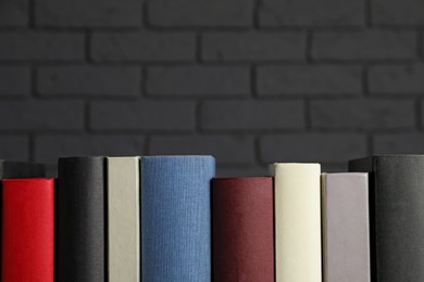 Photo of Many different hardcover books near dark brick wall, space for text