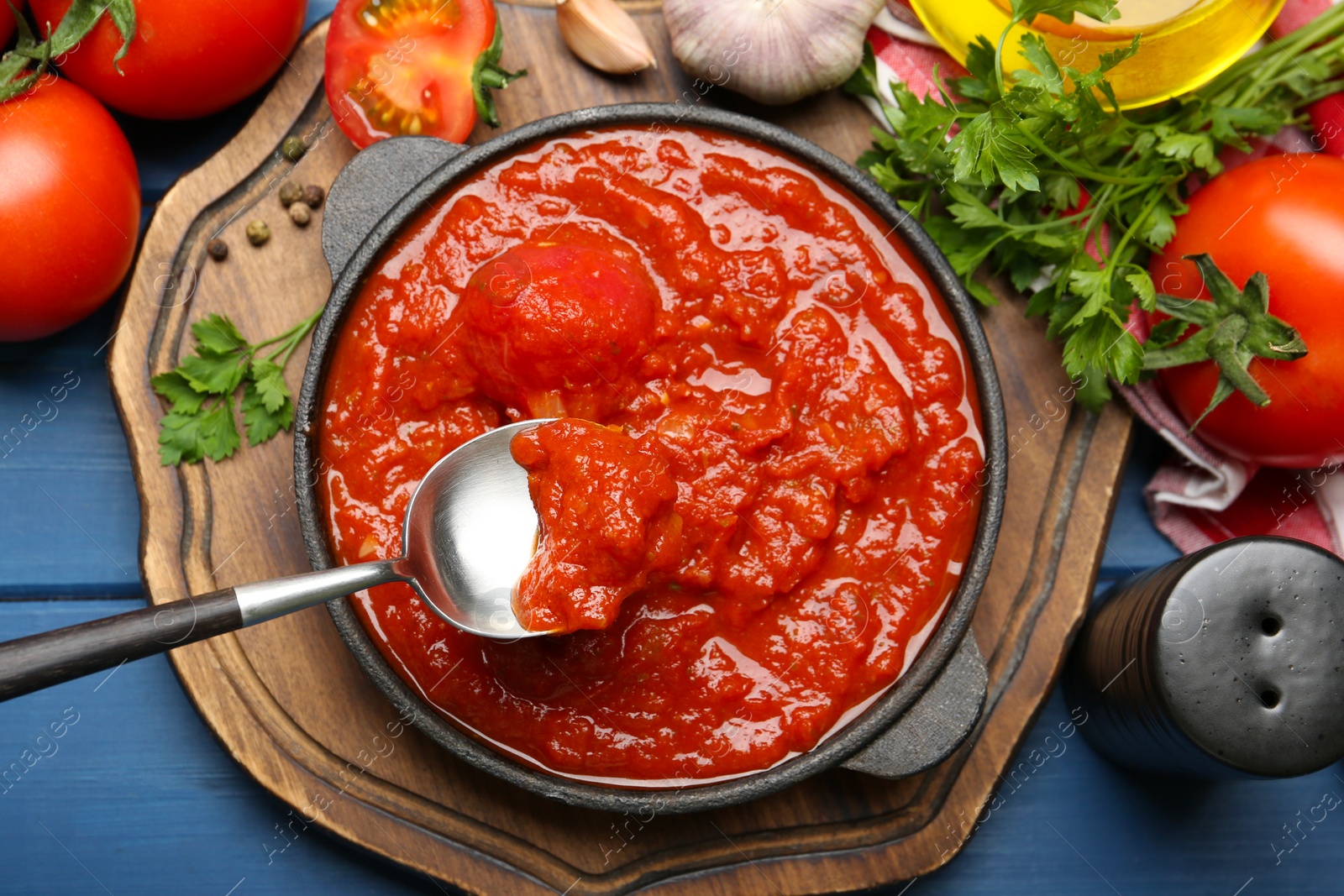 Photo of Homemade tomato sauce in bowl, spoon and ingredients on blue wooden table, flat lay