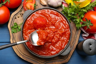 Photo of Homemade tomato sauce in bowl, spoon and ingredients on blue wooden table, flat lay