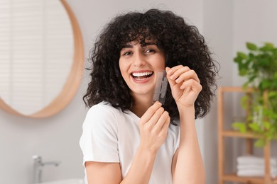 Photo of Young woman holding teeth whitening strips in bathroom