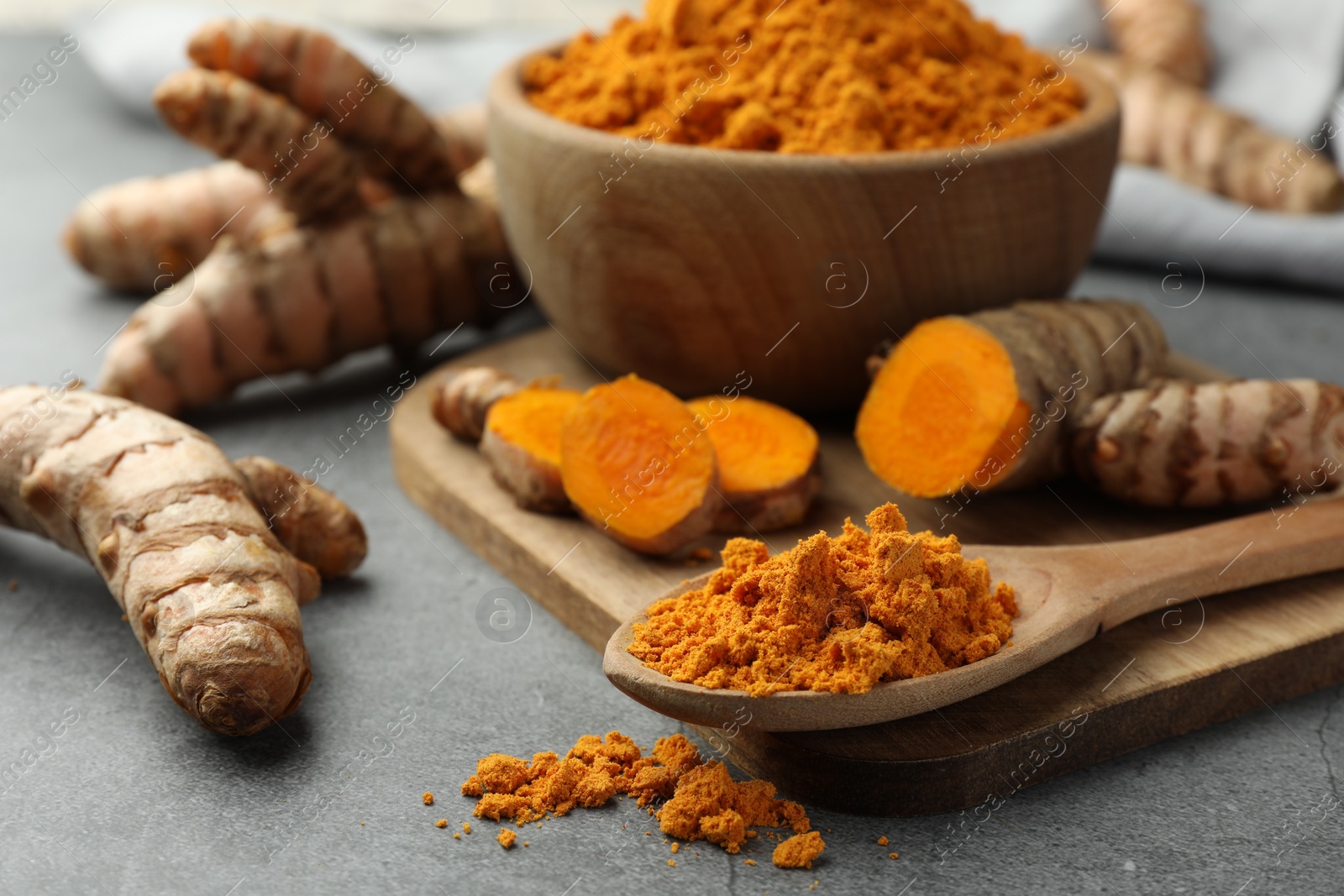 Photo of Aromatic turmeric powder and raw roots on grey table, closeup