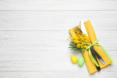 Top view of cutlery set with eggs and floral decor on white wooden table, space for text. Easter celebration