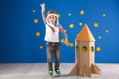 Cute little child playing with cardboard rocket near blue wall
