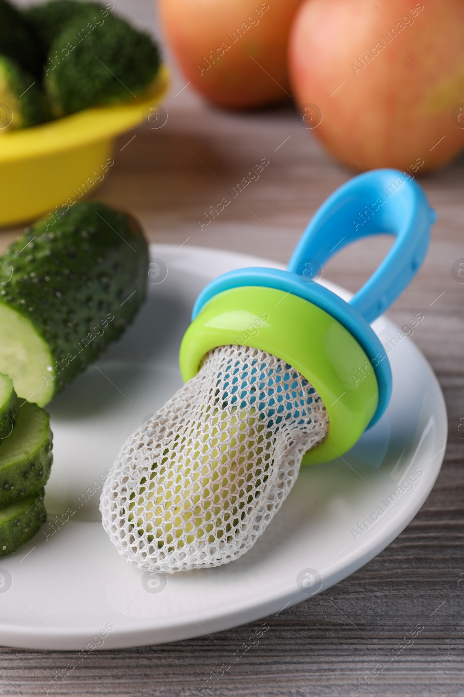 Photo of Nibbler with fresh cucumber on white wooden table. baby feeder