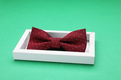 Photo of Stylish burgundy bow tie with polka dot pattern in box on green background