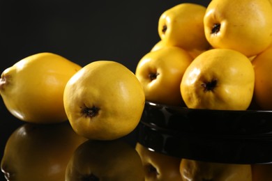 Photo of Tasty ripe quinces in bowl on black mirror surface, closeup