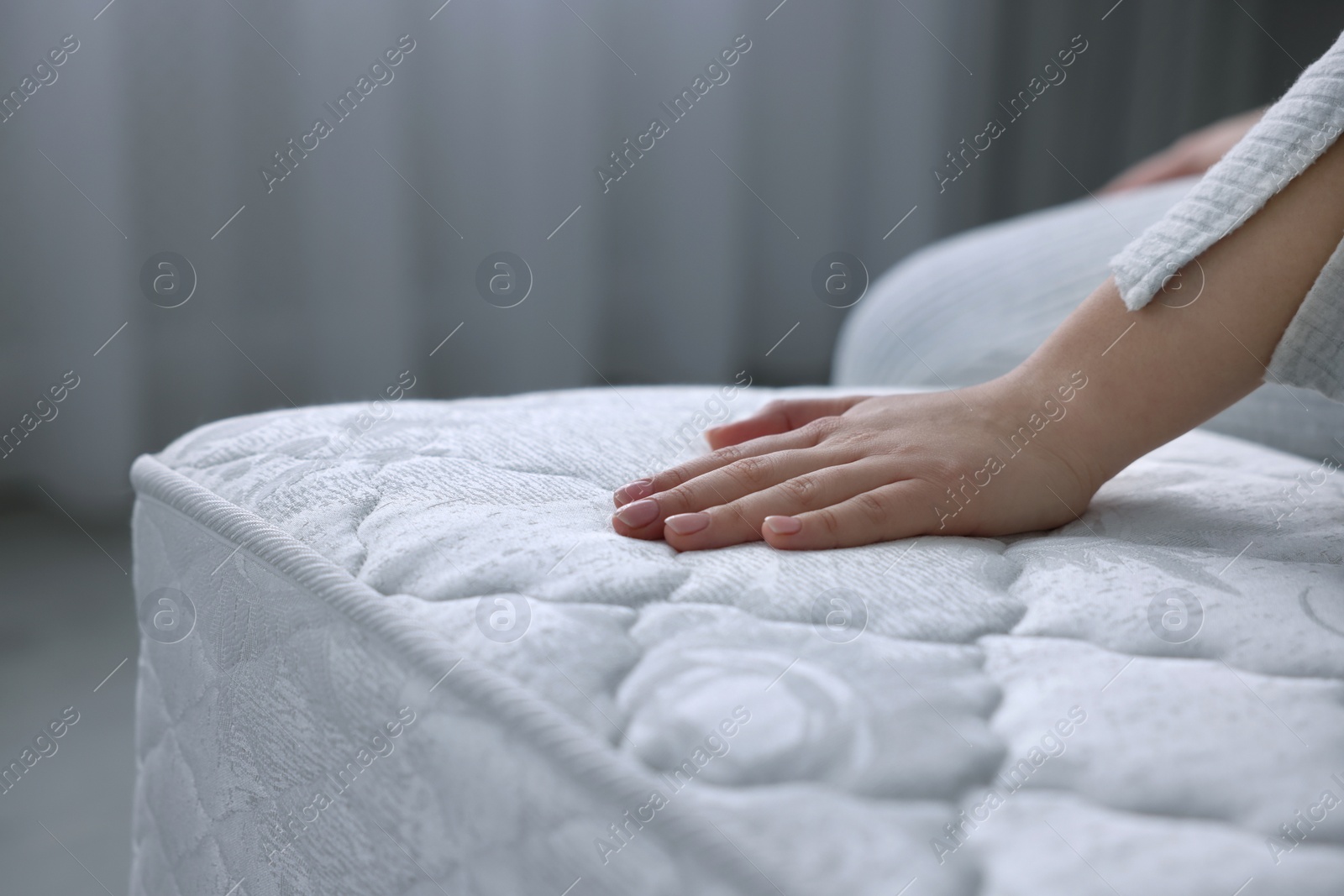 Photo of Woman touching soft white mattress indoors, closeup