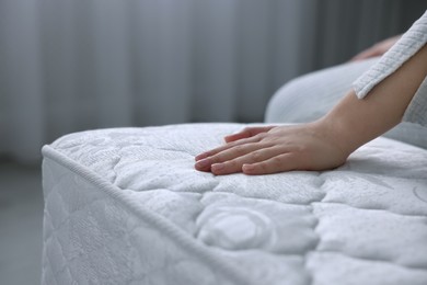 Woman touching soft white mattress indoors, closeup