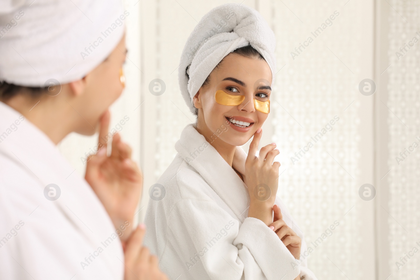 Photo of Beautiful young woman with under eye patches near mirror at home