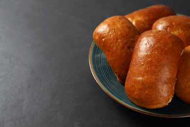 Photo of Delicious baked pirozhki on black table, closeup. Space for text