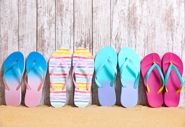 Photo of Different bright flip flops on sand near wooden wall, space for text. Summer beach accessories