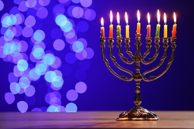Photo of Hanukkah celebration. Menorah with burning candles on table against blue background with blurred lights, space for text