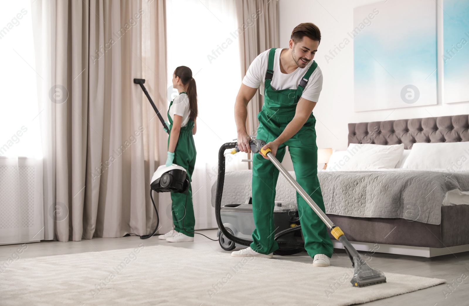 Photo of Team of janitors cleaning bedroom with professional equipment