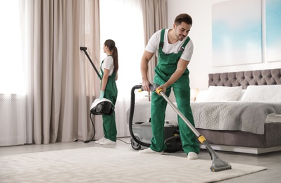 Photo of Team of janitors cleaning bedroom with professional equipment