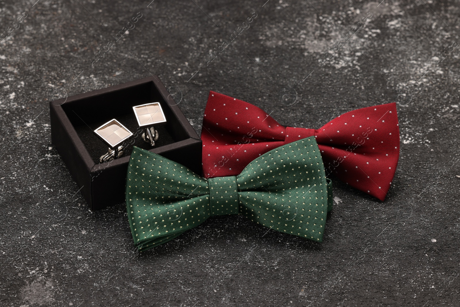 Photo of Stylish color bow ties and box of cufflinks on grey textured background
