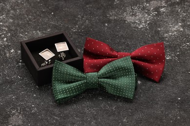 Photo of Stylish color bow ties and box of cufflinks on grey textured background
