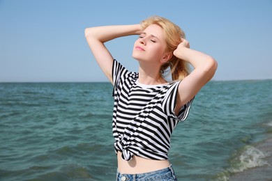 Beautiful young woman near sea on sunny day in summer