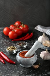 Photo of Mortar with red curry paste and ingredients on black textured table