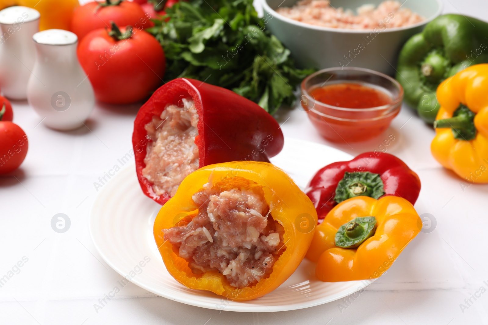 Photo of Raw stuffed peppers, ground meat and ingredients on white table