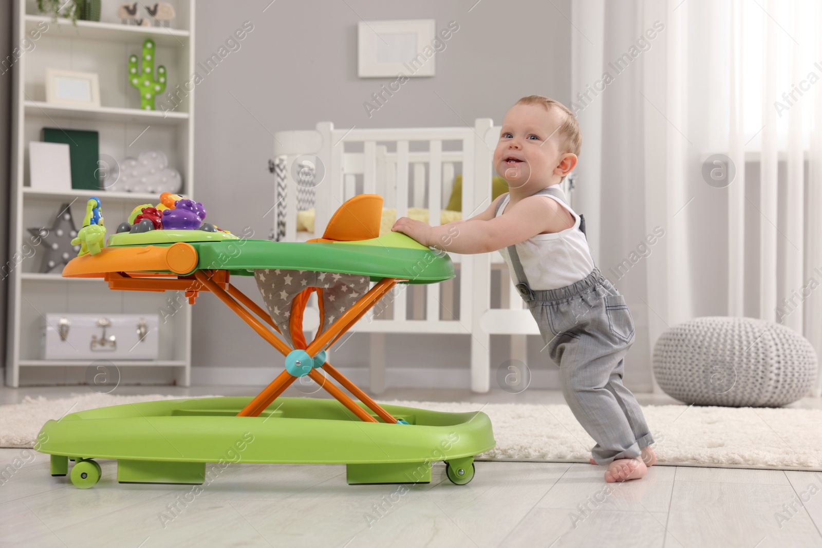 Photo of Cute baby making first steps with toy walker at home