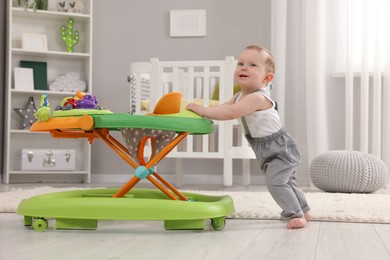 Photo of Cute baby making first steps with toy walker at home