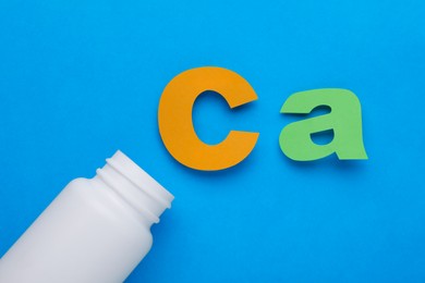 Photo of Open bottle and calcium symbol made of colorful letters on light blue background, flat lay