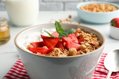 Photo of Bowl with tasty granola and strawberries on white table, closeup. Healthy meal